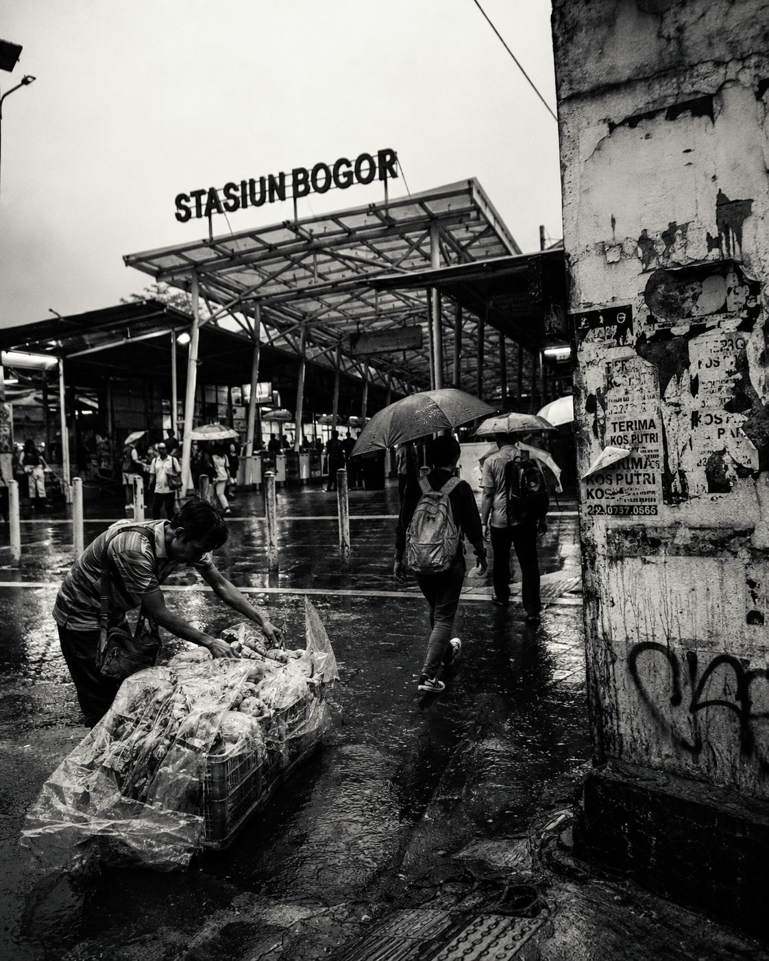 pedagang menjadi pusat diam dari seluruh keramaian. Sementara orang-orang bergerak menuju stasiun, ia justru menunduk, merapikan barang, memastikan plastik tetap menutup dagangan.  Ada sesuatu yang sangat kuat dari gestur kecil ini. Tidak heroik, tidak dramatis, tapi nyata. Di tengah hujan dan arus penumpang, ia tidak tampil sebagai korban kota. Ia adalah bagian dari mesin kota yang tidak pernah benar-benar berhenti. #streetfoto